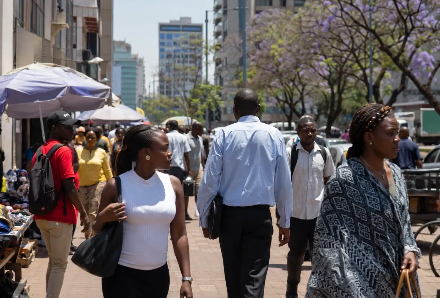 A pavement in central Harare on a weekday morning, with market umbrellas and jacaranda trees